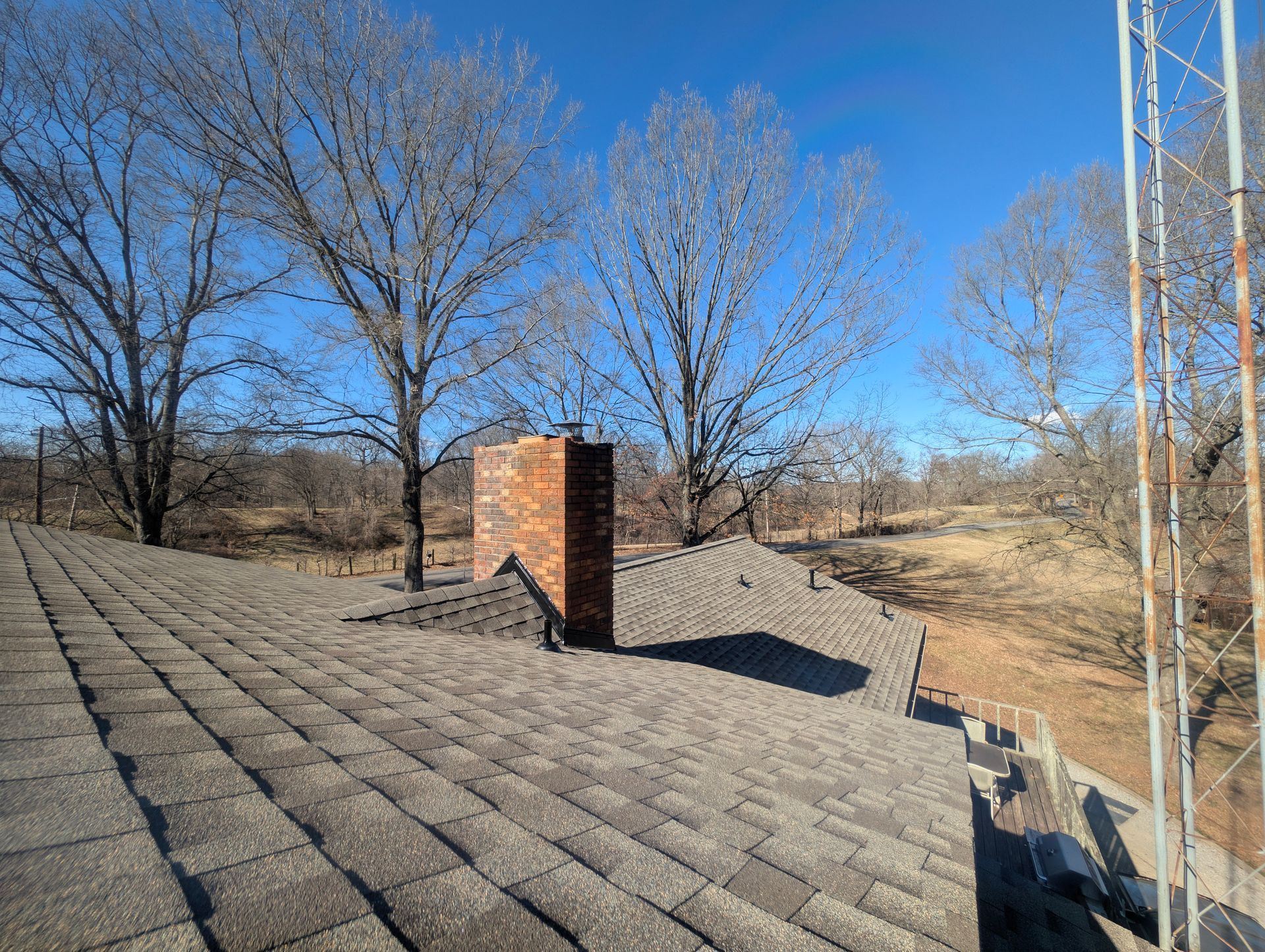 Rooftop with brick chimney, trees, and metal structure on a sunny day.