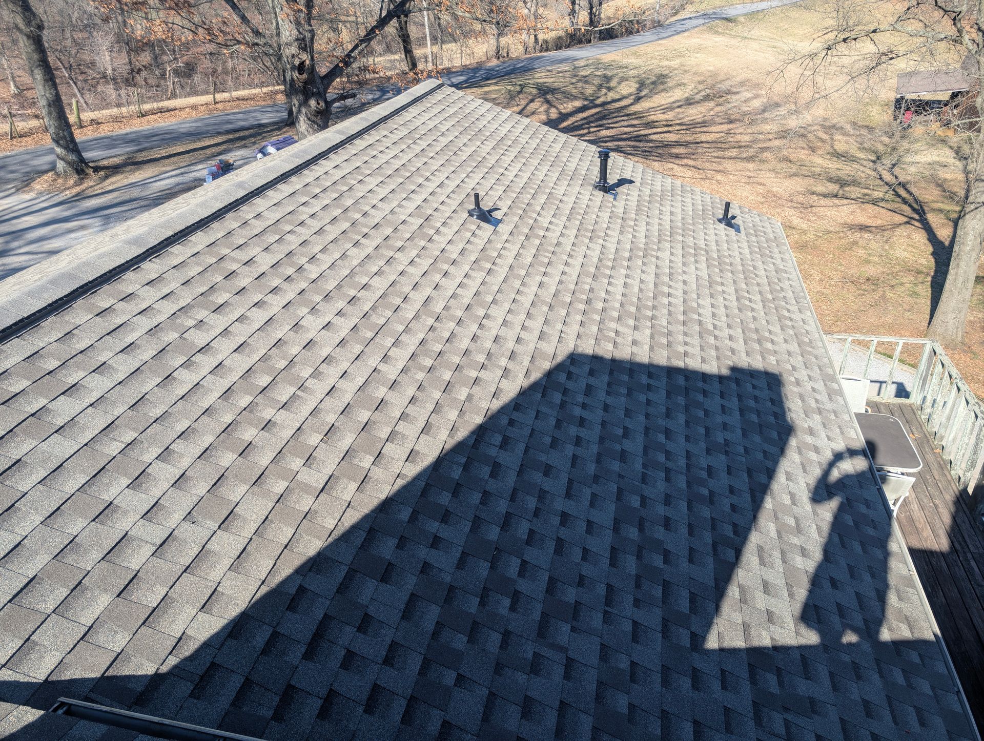 Overhead view of a gray shingle roof with a shadow of a person holding a camera on the deck.