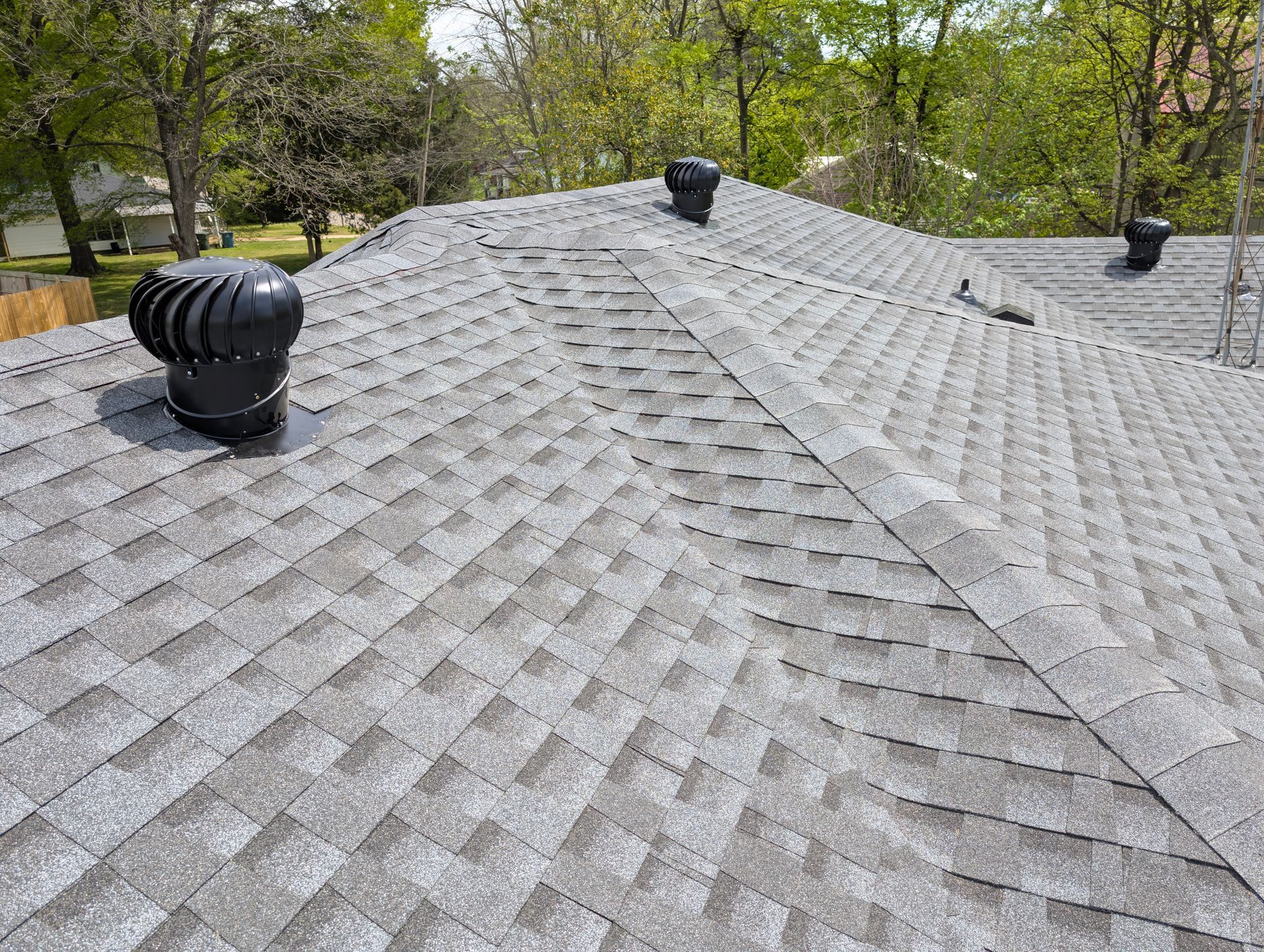 Gray asphalt shingle roof with three black turbine vents, trees visible in the background.