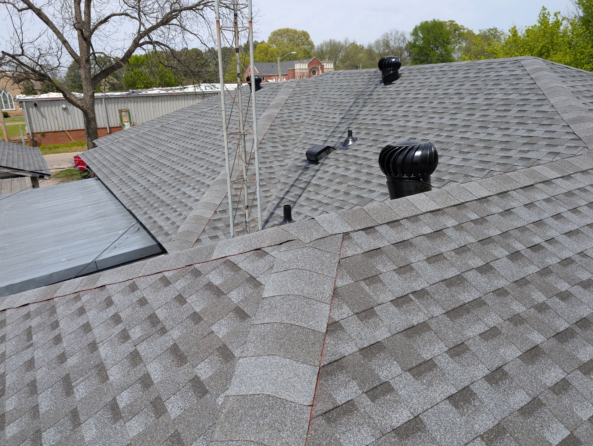 Gray shingled roof with a vent and antenna in a residential setting.