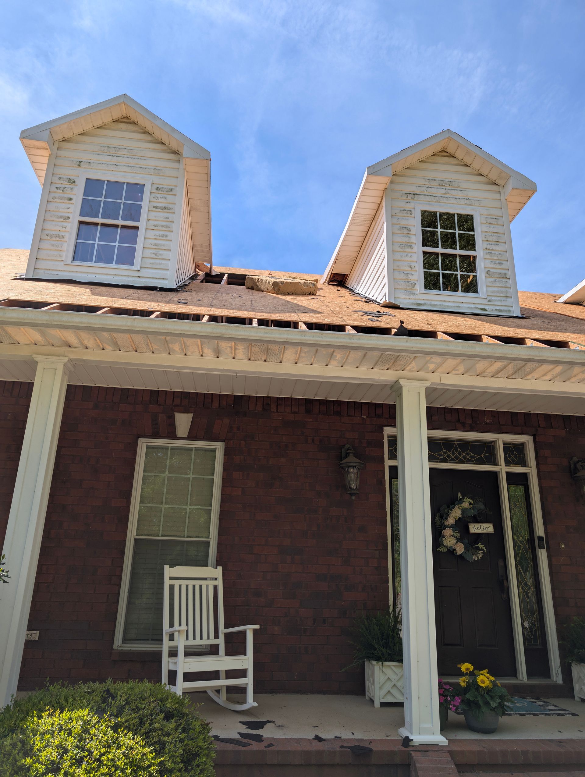 A house with two dormers and a porch, roof partially exposed, under a blue sky.