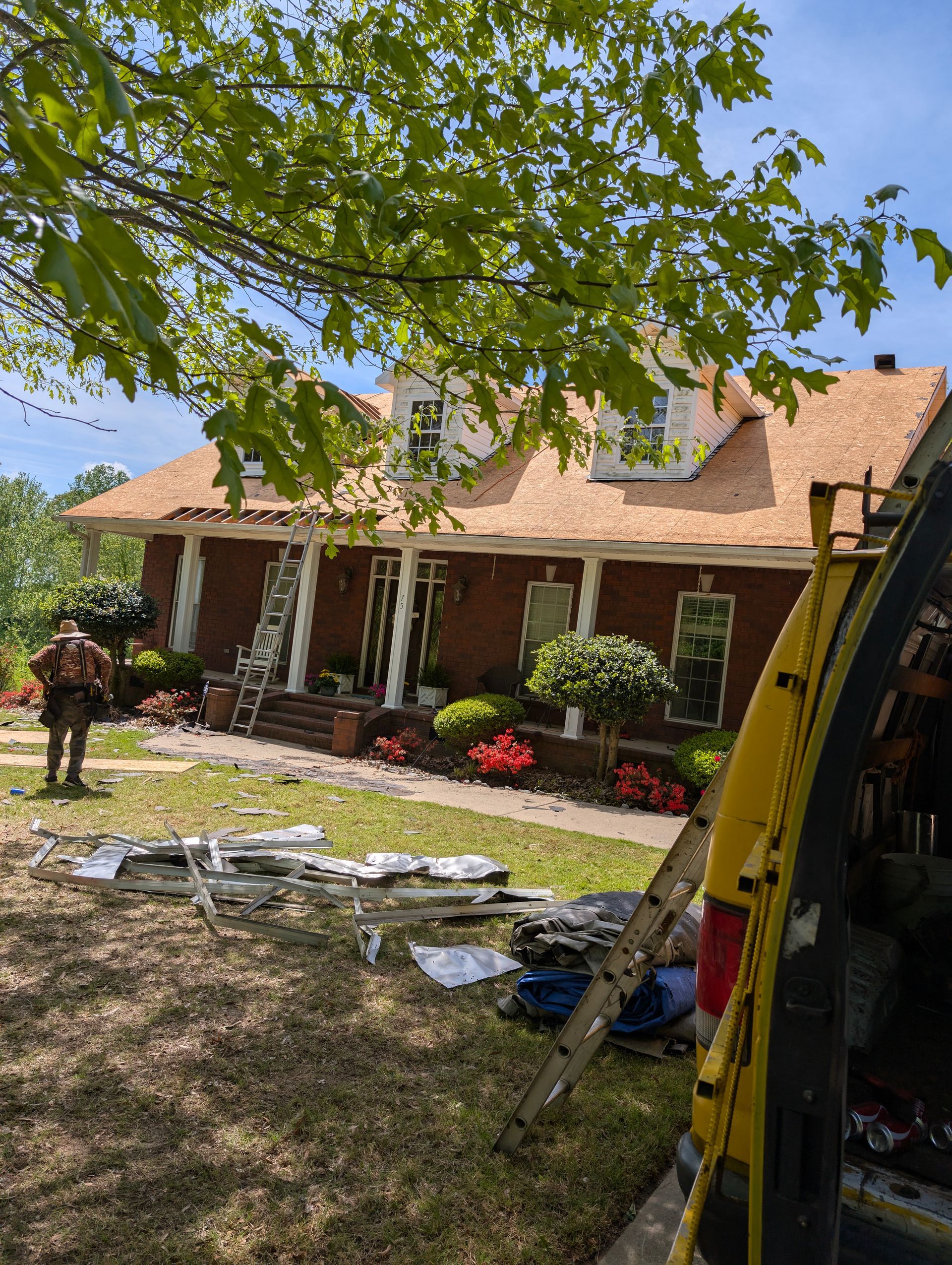 House with new roof under construction; worker, ladder, and tools in yard.