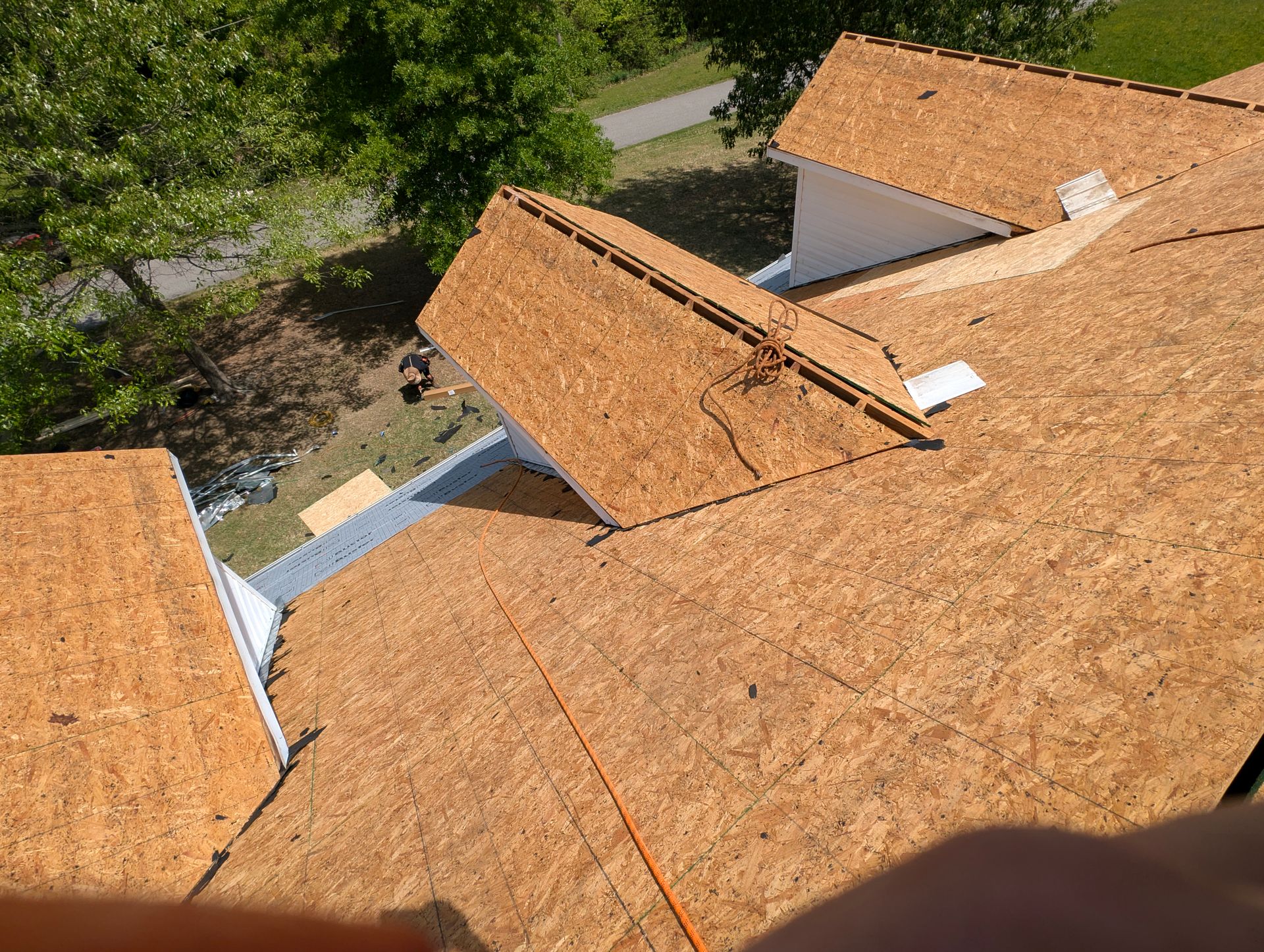 New roof installation: OSB sheathing on multiple roof planes; safety rope visible.