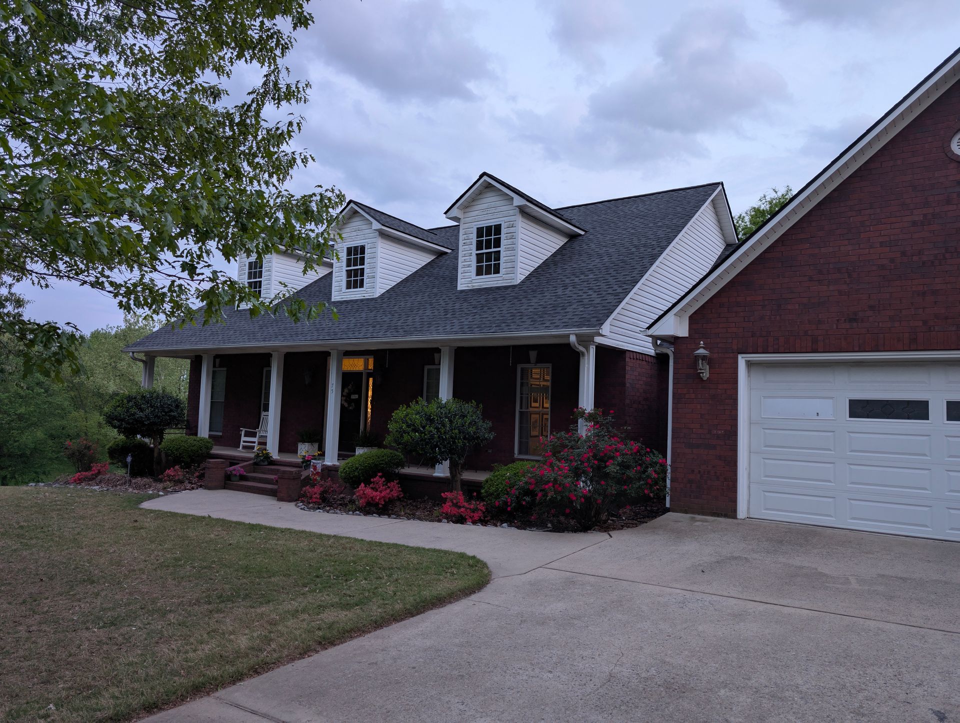 Brick house with white trim, dormers, and a two-car garage under a cloudy sky.