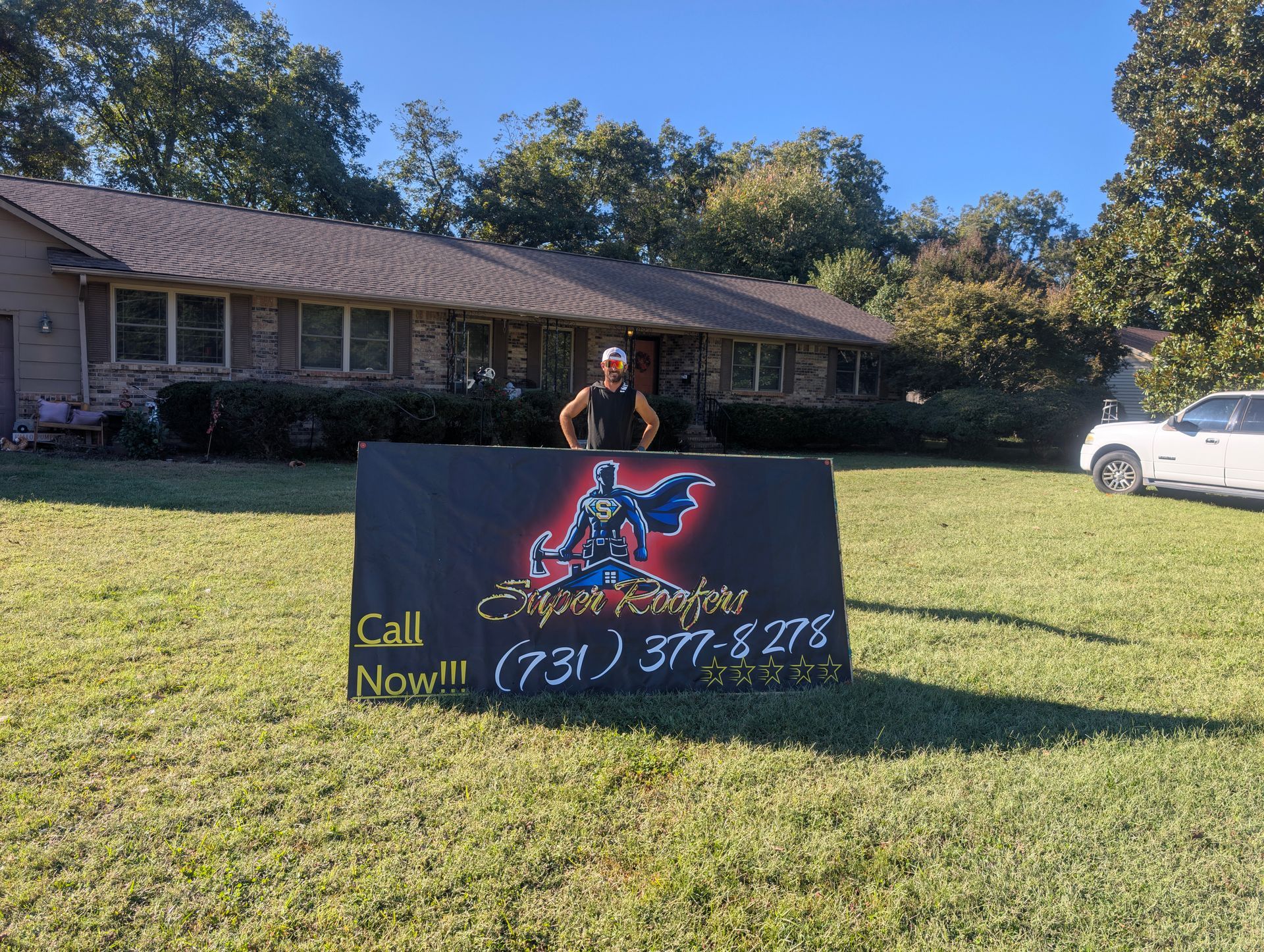 Man standing behind a sign with a logo and phone number, in front of a house.