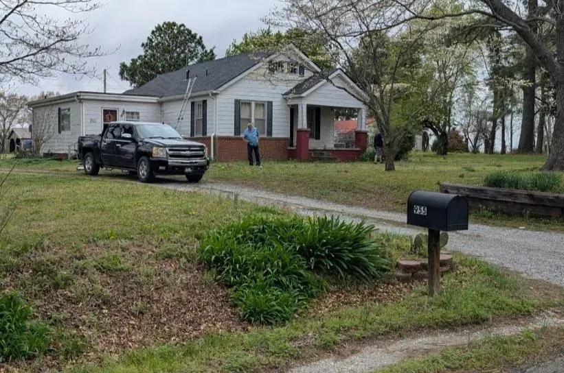 Pickup truck parked in front of a white house with a person standing on the porch. Driveway and mailbox.