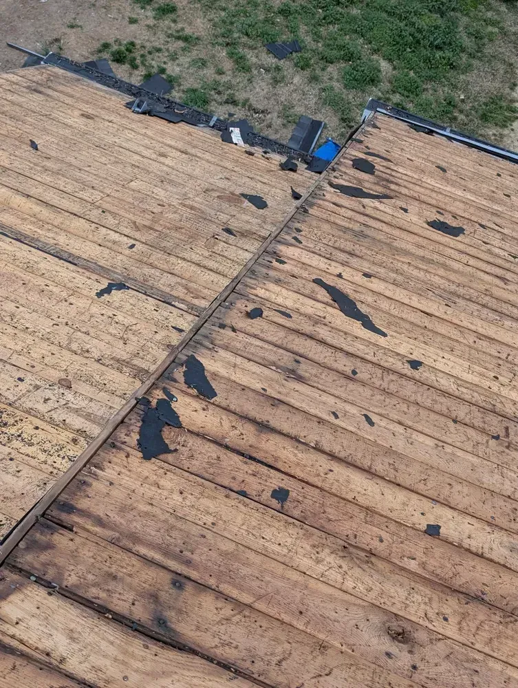 Overhead view of a wooden roof with dark spots, possibly water damage, and a blue drain.