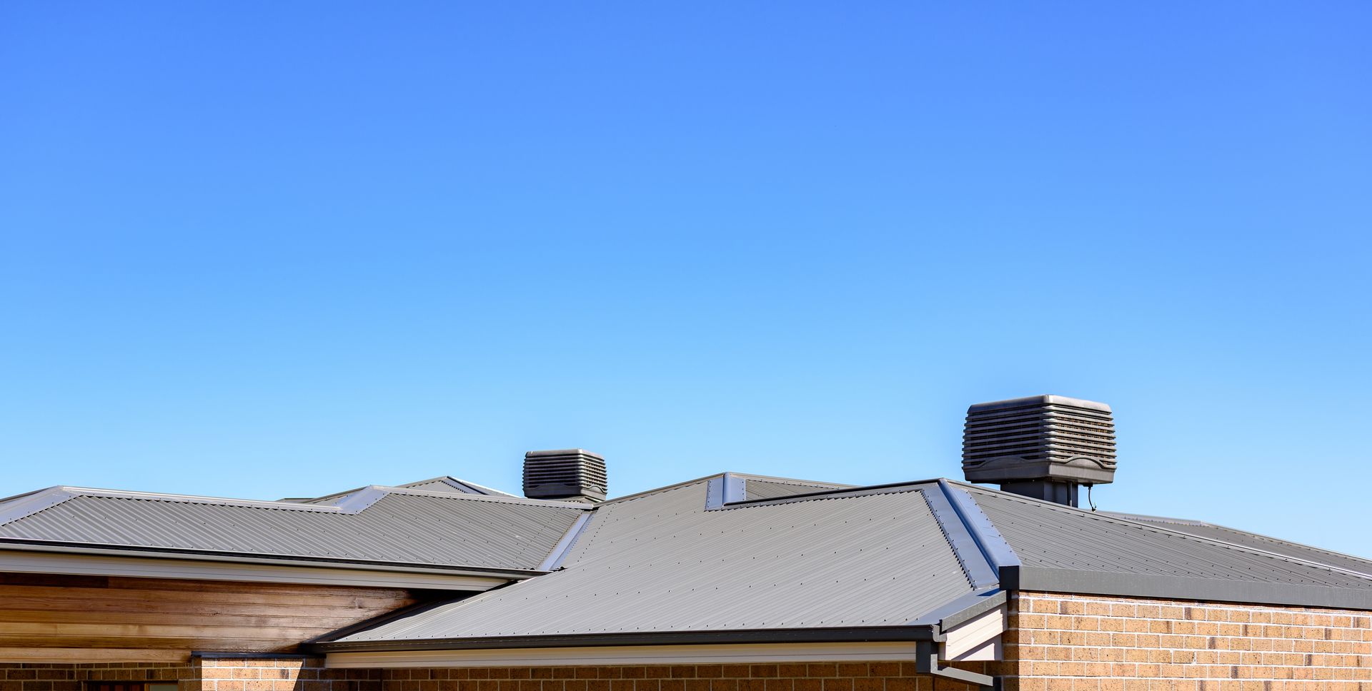 Roof of a house with a gray metal roof, against a clear blue sky.