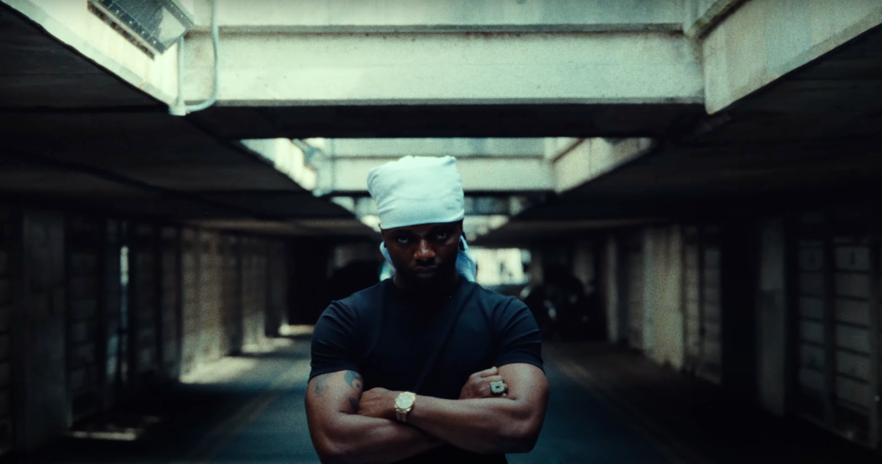 A man with a bandana on his head is standing in a dark tunnel with his arms crossed.