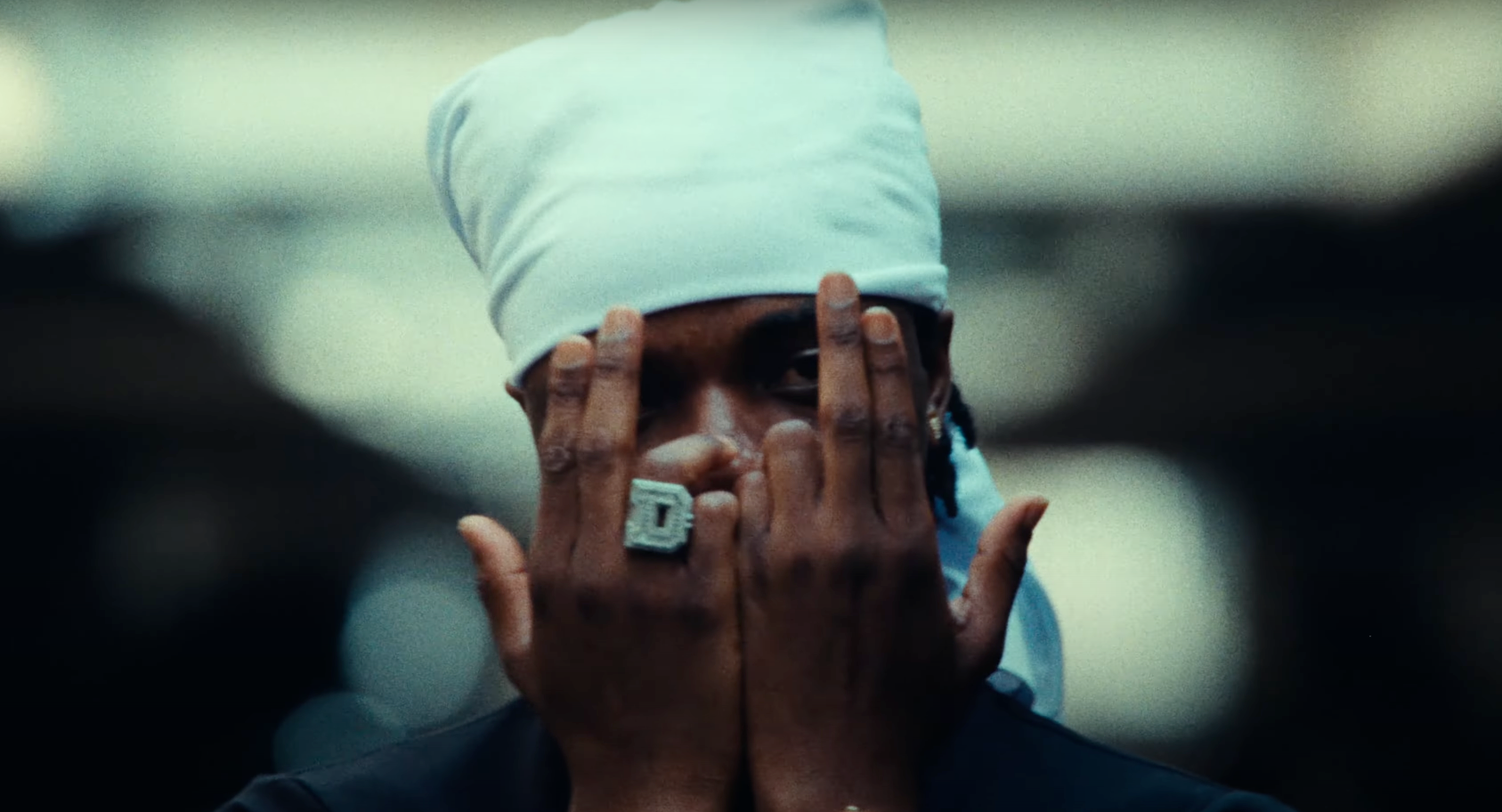 A man wearing a bandana and a ring is covering his face with his hands.