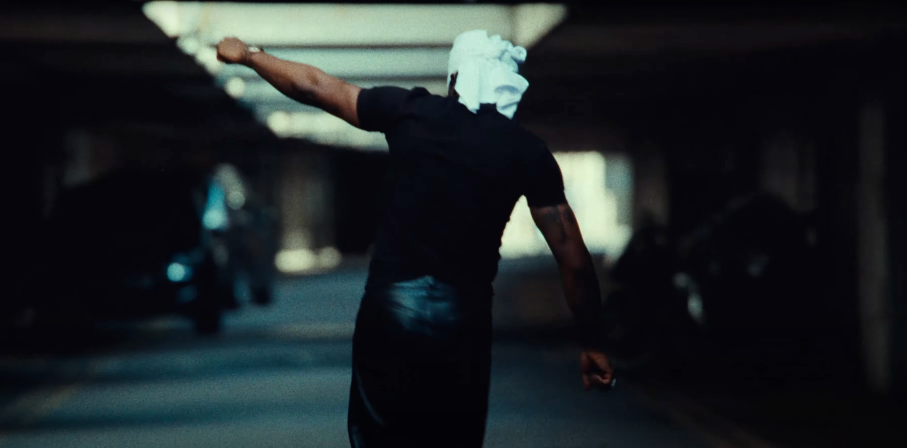 A man with a bandana on his head is walking down a dark street.