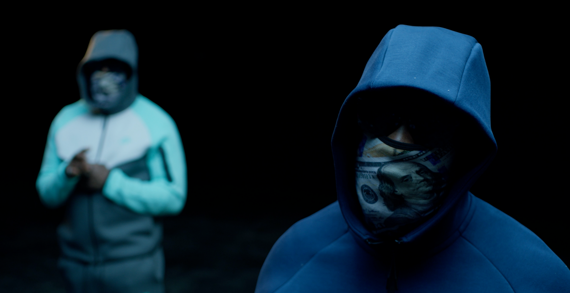 Two men in hoodies and masks are standing next to each other in the dark.