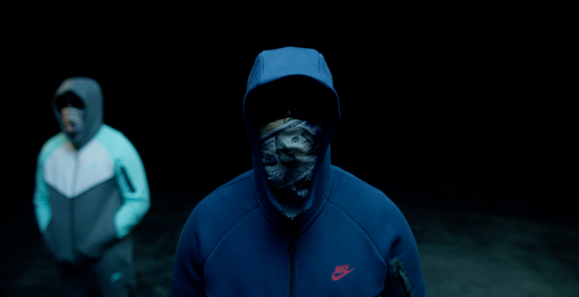 Two men wearing hoodies and masks are standing next to each other in the dark.