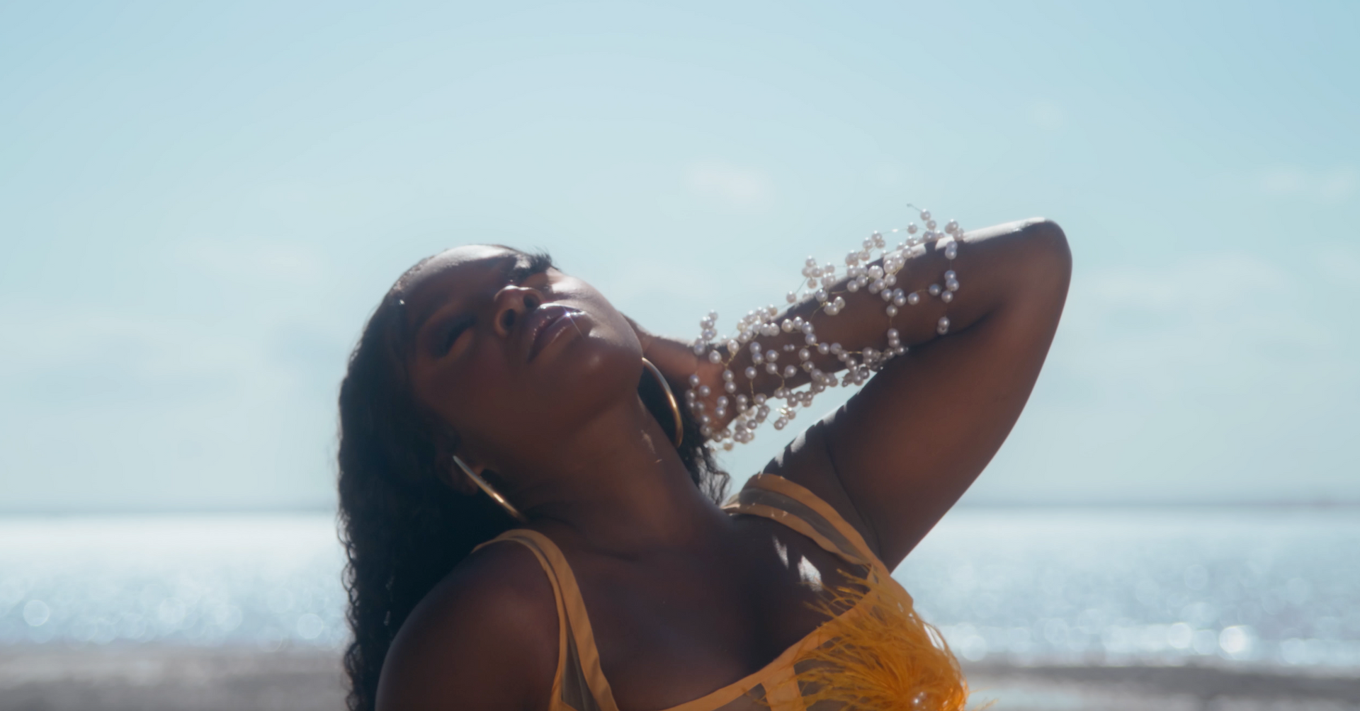 A woman in a yellow dress is standing on a beach with water coming out of her hair.