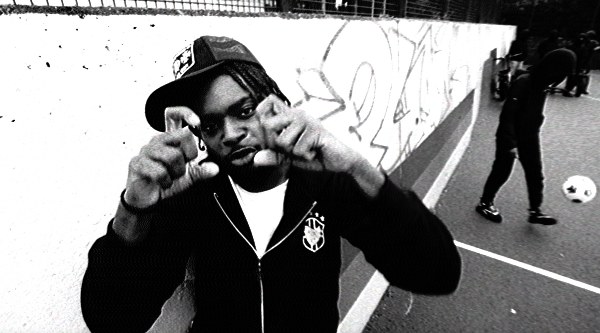 A black and white photo of a man wearing a hat pointing at the camera.