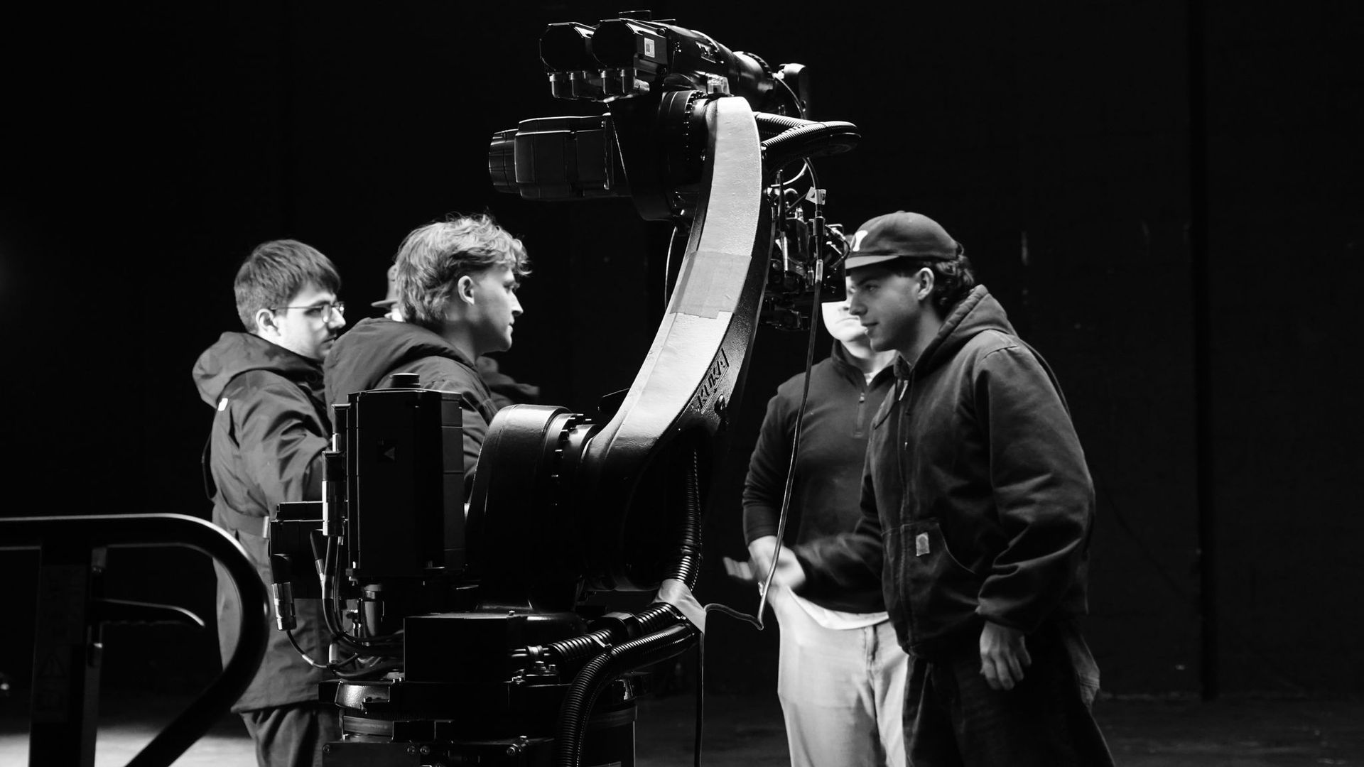 A group of people are standing around a camera in a black and white photo.