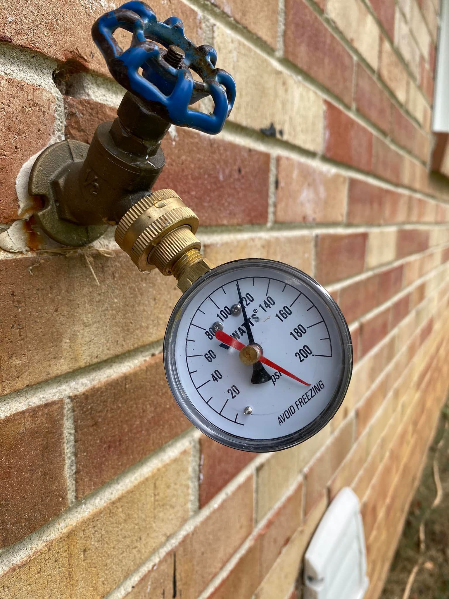 A Pressure Gauge Is Attached to A Faucet on A Brick Wall - Bristol, TN - Austin’s Plumbing, LLC