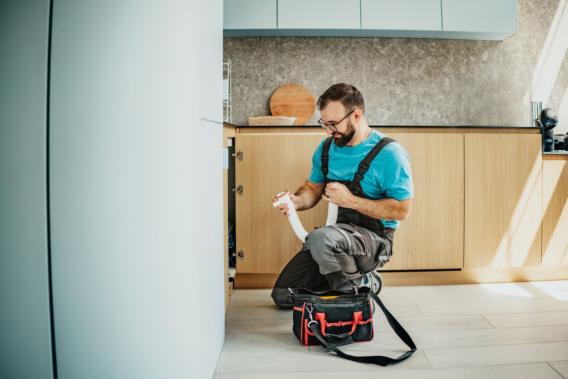 Plumbing repair contractors fixing kitchen sink with tools and tape in modern home interior.