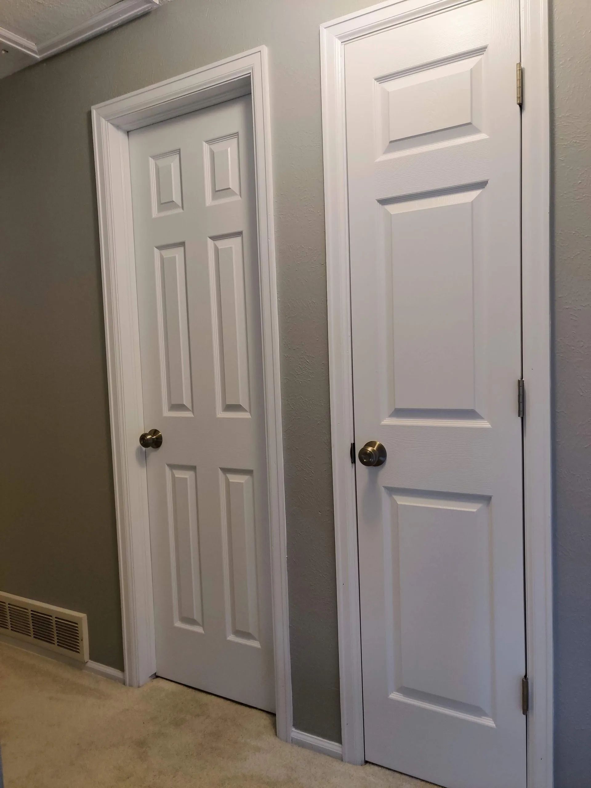 Two white paneled doors with white trim, on a gray wall in a hallway.