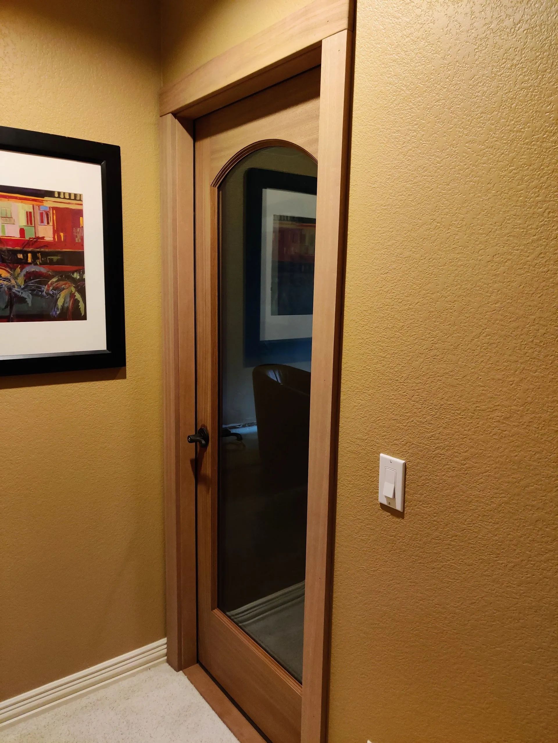 Wooden door with arched top, framed by light wood, opening into a room with a painting visible. Yellow textured walls.