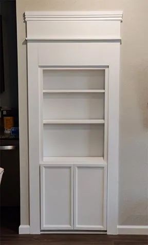 White built-in shelving unit featuring three open shelves above a cabinet with two shaker-style doors.