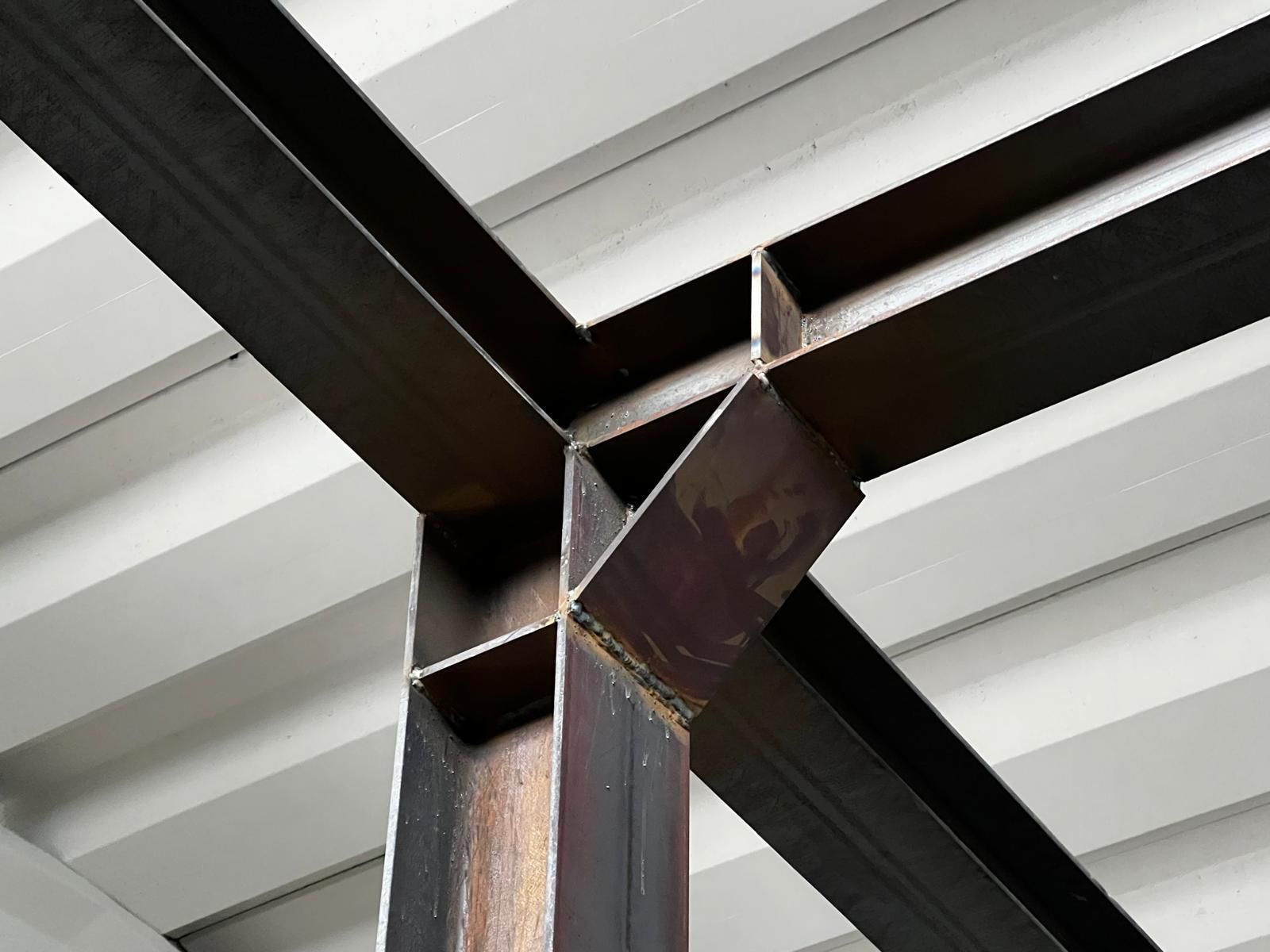 Primo piano di travi in acciaio saldate con controvento diagonale su un soffitto metallico bianco.