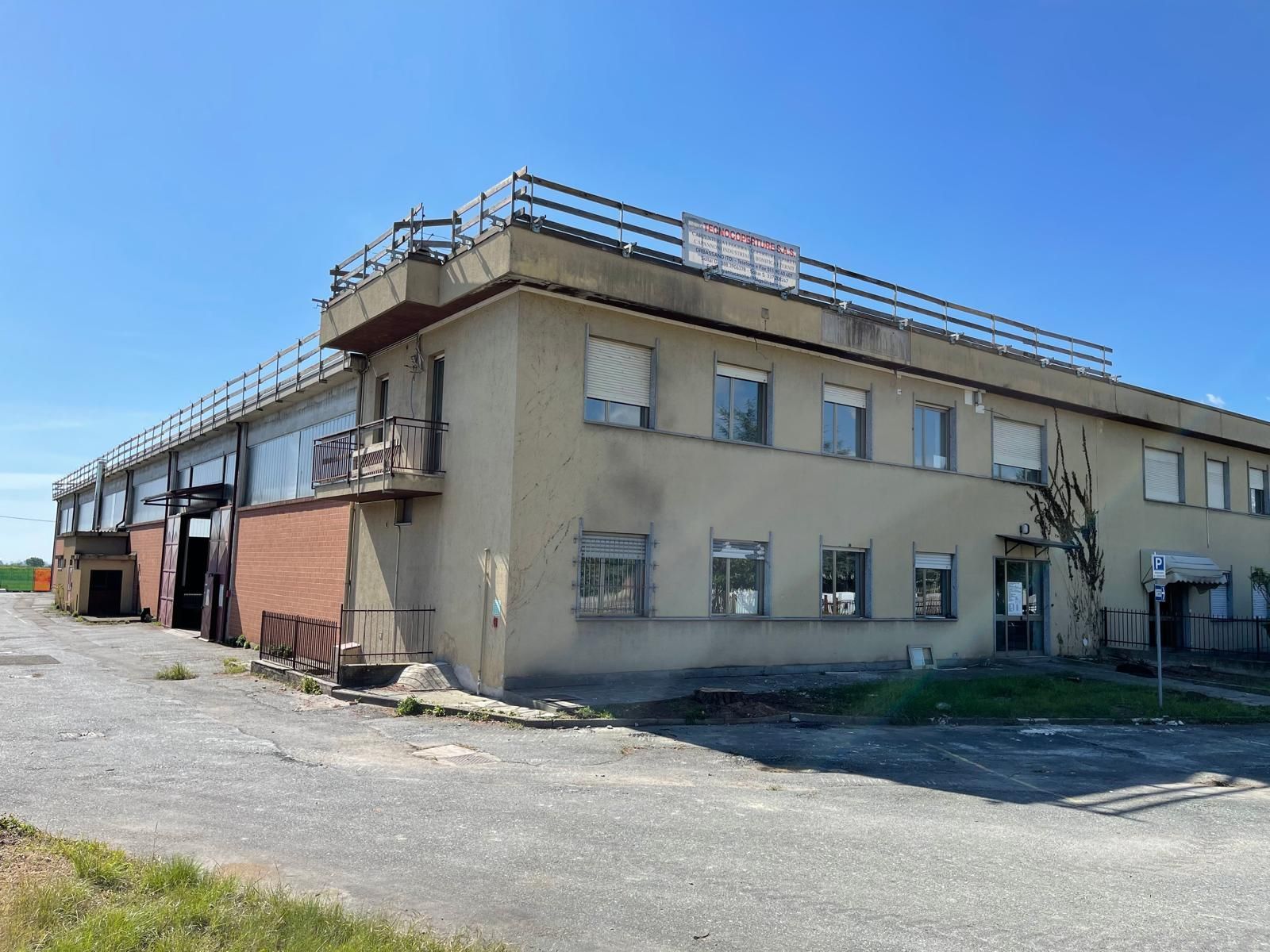 Edificio industriale di colore beige basso con ringhiere sul tetto sotto un cielo azzurro limpido.