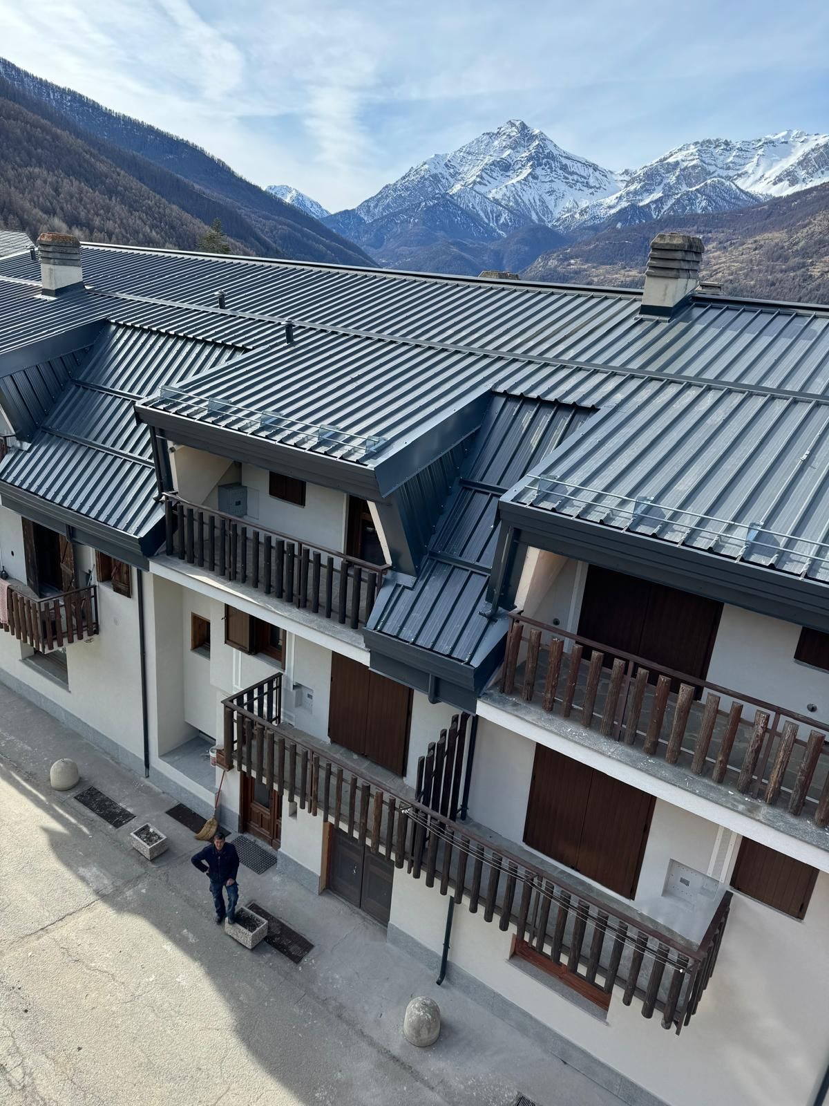 Chalet alpino con tetti e balconi grigi, sullo sfondo di montagne innevate sotto un cielo limpido.