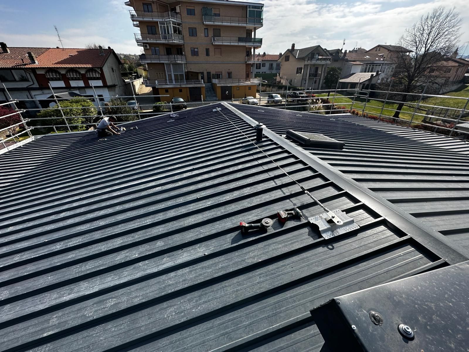 Tetto con pannelli ondulati scuri e una scala, con vista su palazzi e alberi.