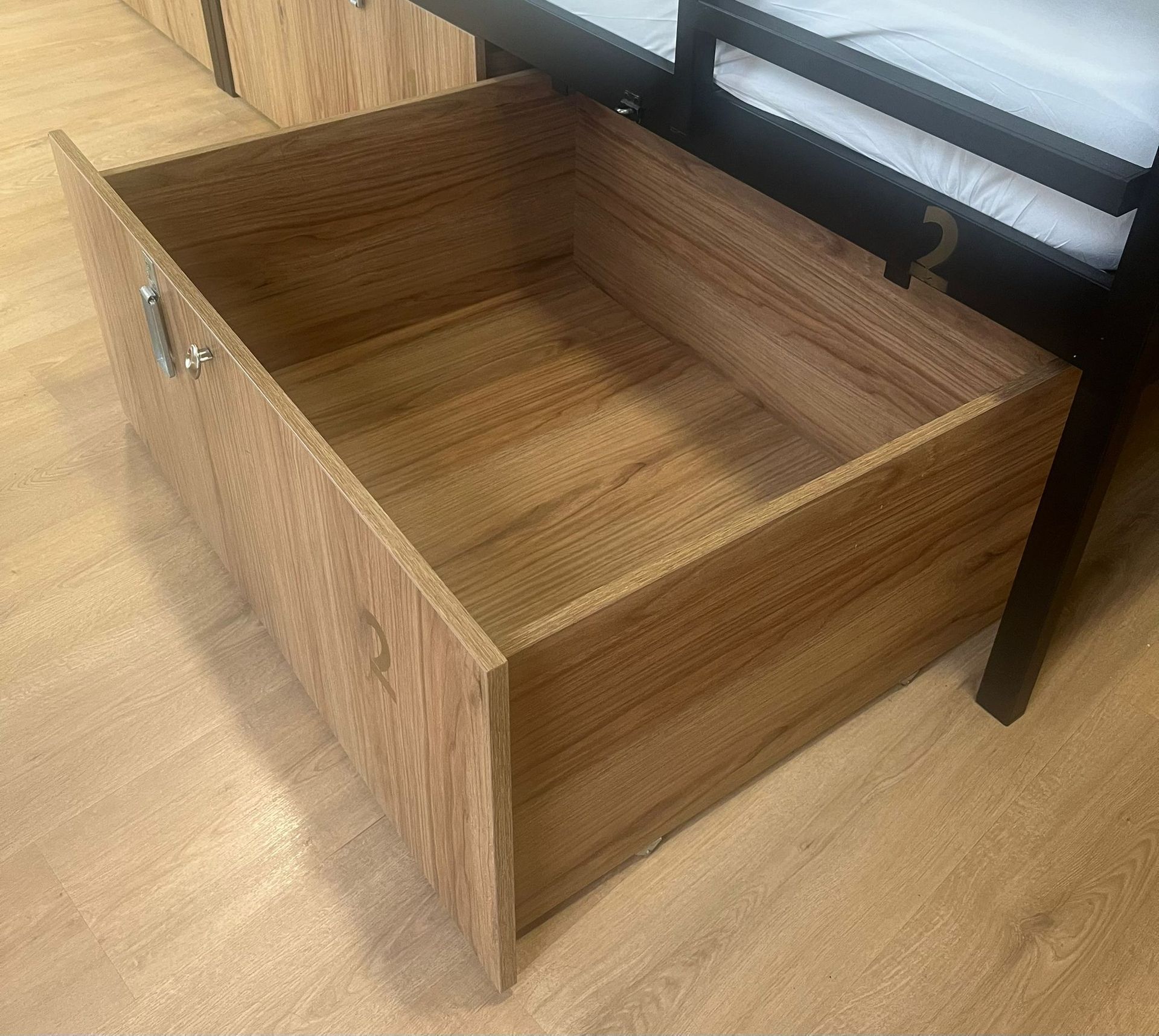 Cajón de madera abierto debajo de una estructura de cama negra.