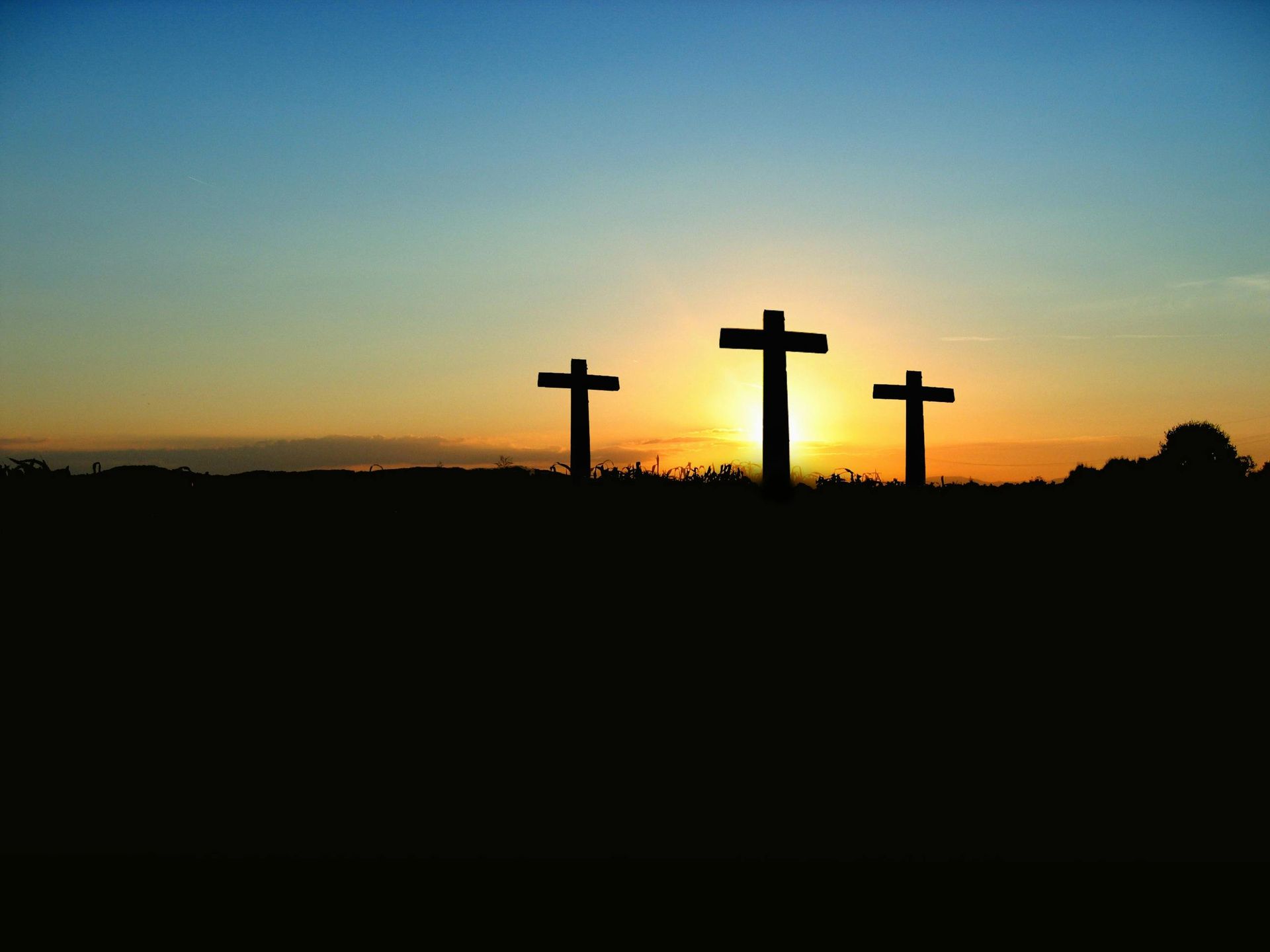 Three silhouetted crosses on a hill with a setting sun in the background.
