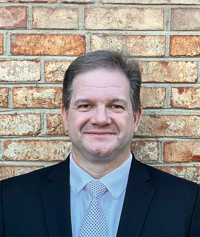 Man in suit and tie smiles in front of a brick wall.