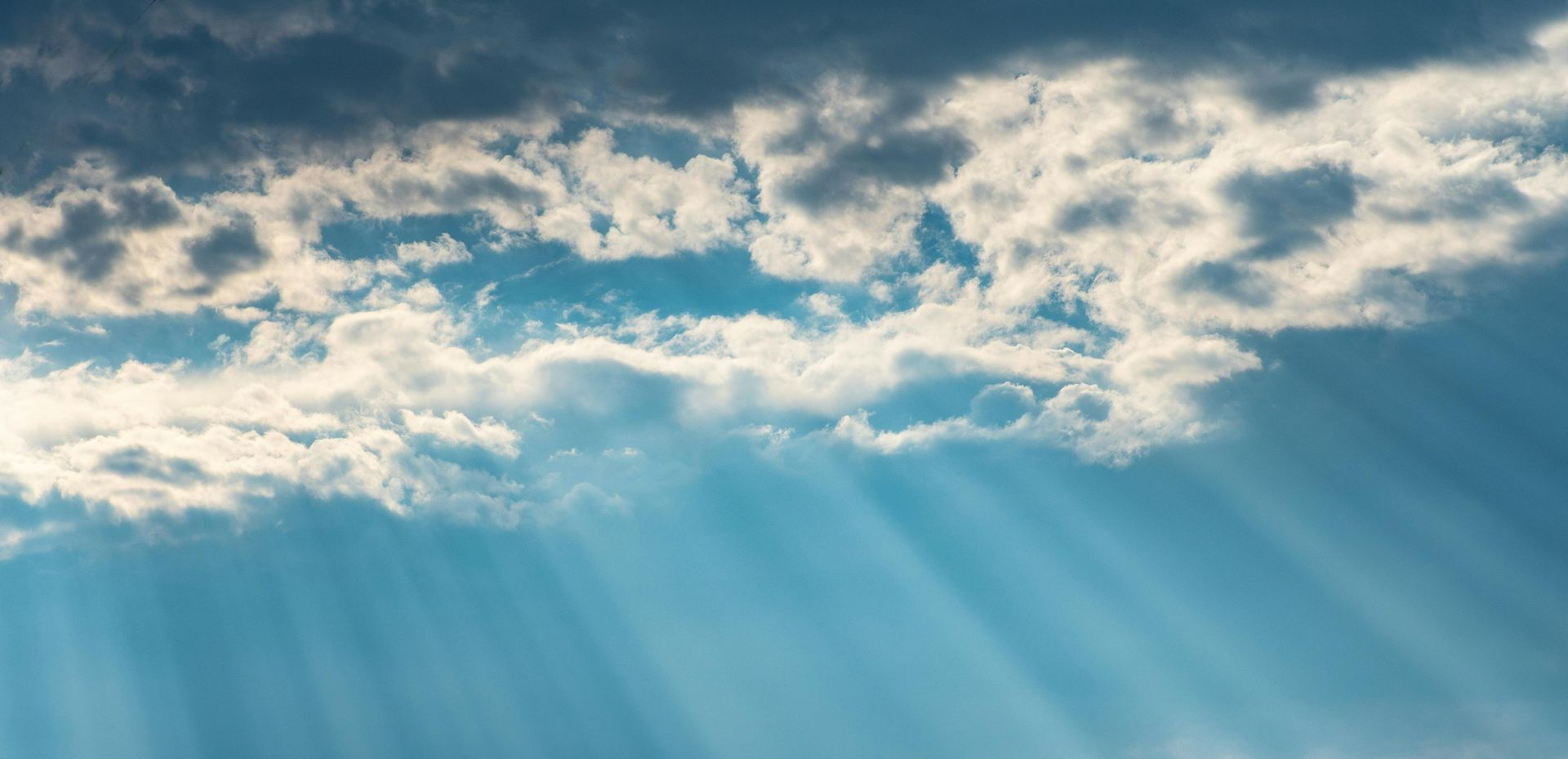 Sunlight streams through clouds in a bright blue sky.
