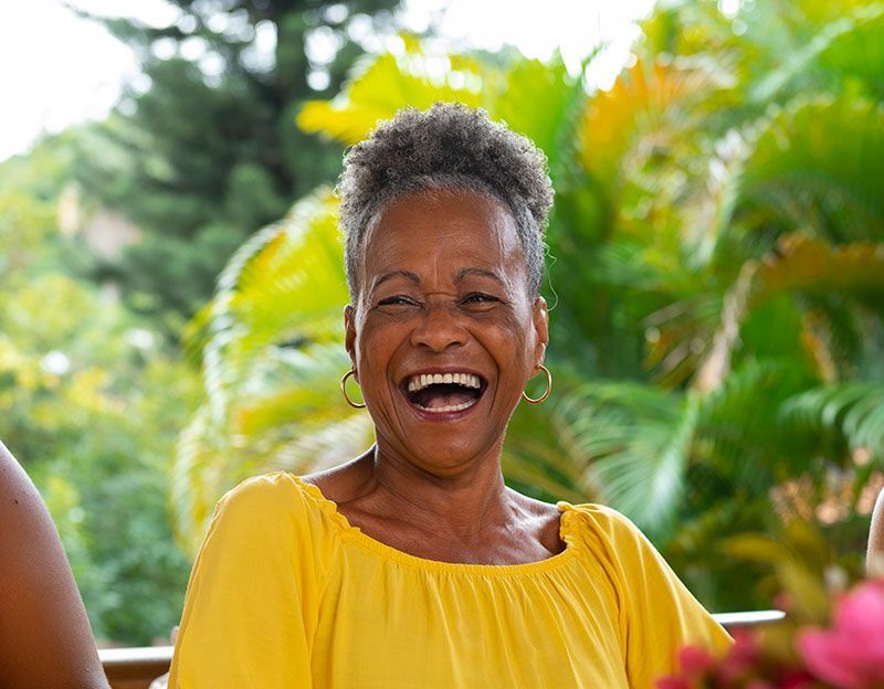 Woman in yellow laughing outdoors with a green backdrop.