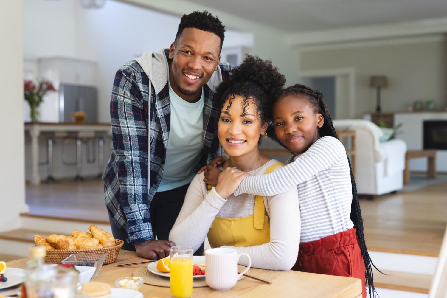 Family smiling together at a breakfast table in a bright kitchen with pastries, juice, and coffee.