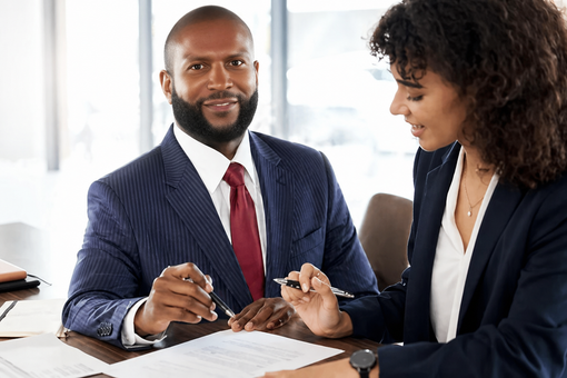 Two colleagues reviewing paperwork together at a desk in a bright office