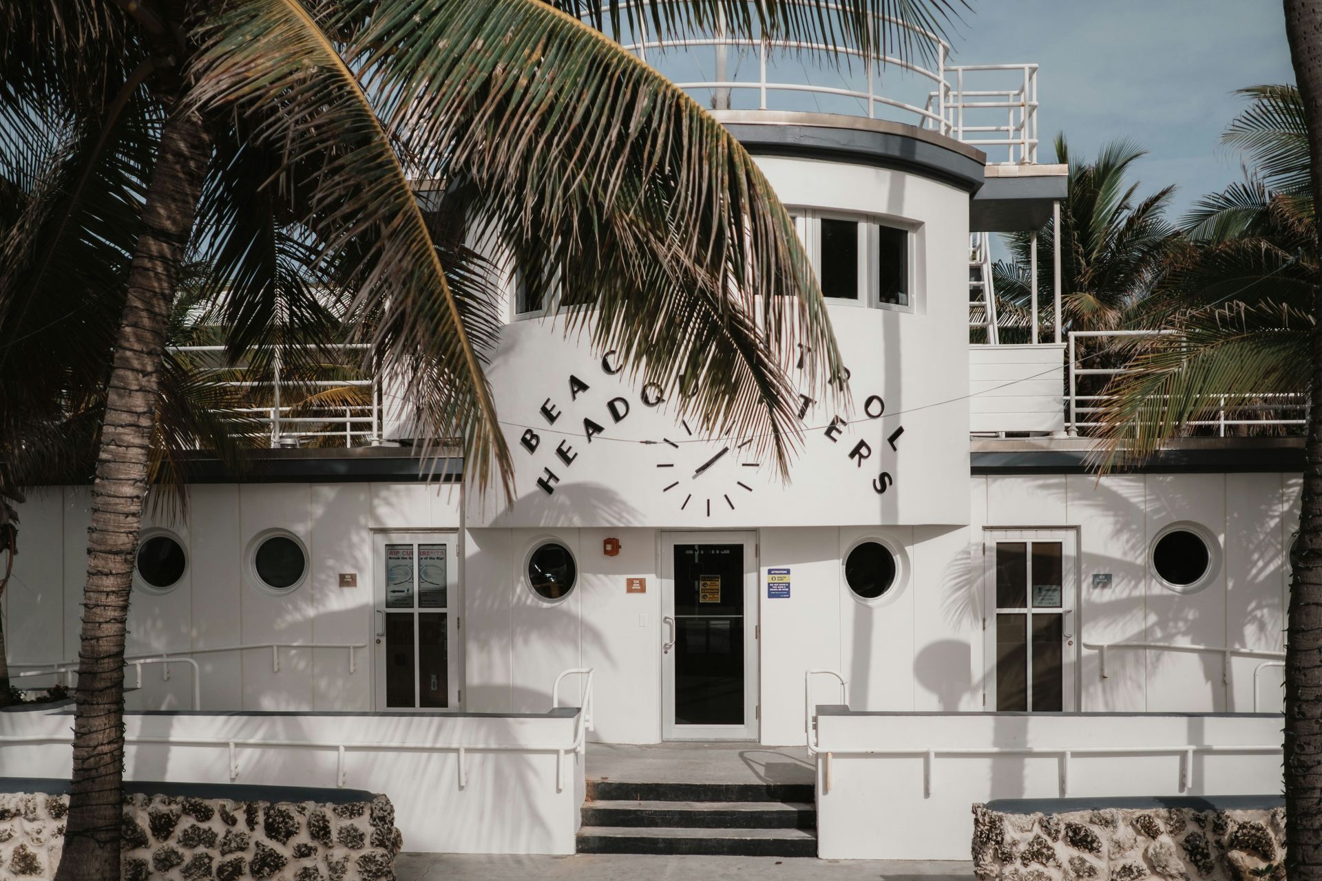 White Art Deco building with palm trees and circular windows, viewed from the front entrance