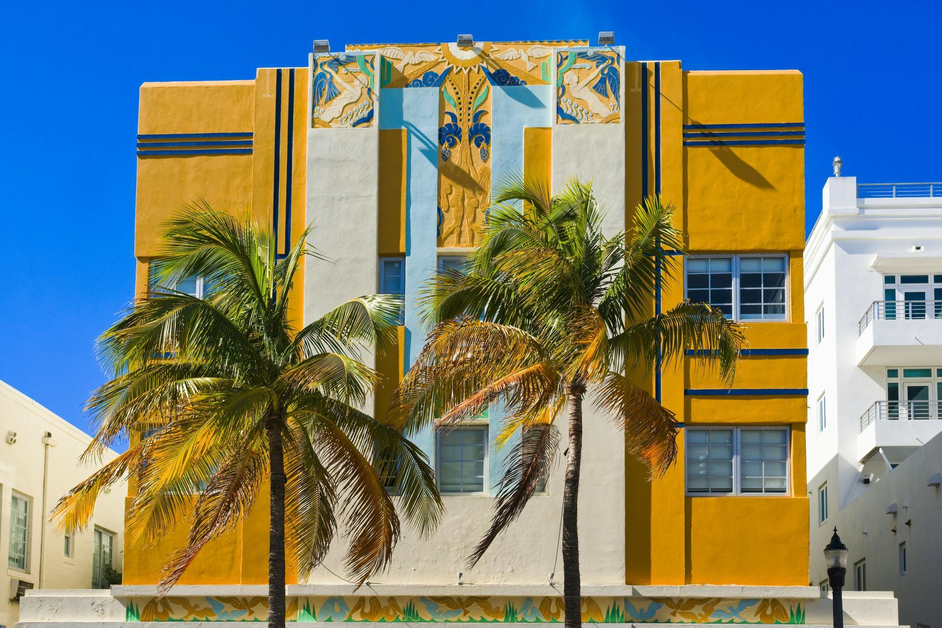 Yellow Art Deco building with palm trees against a bright blue sky