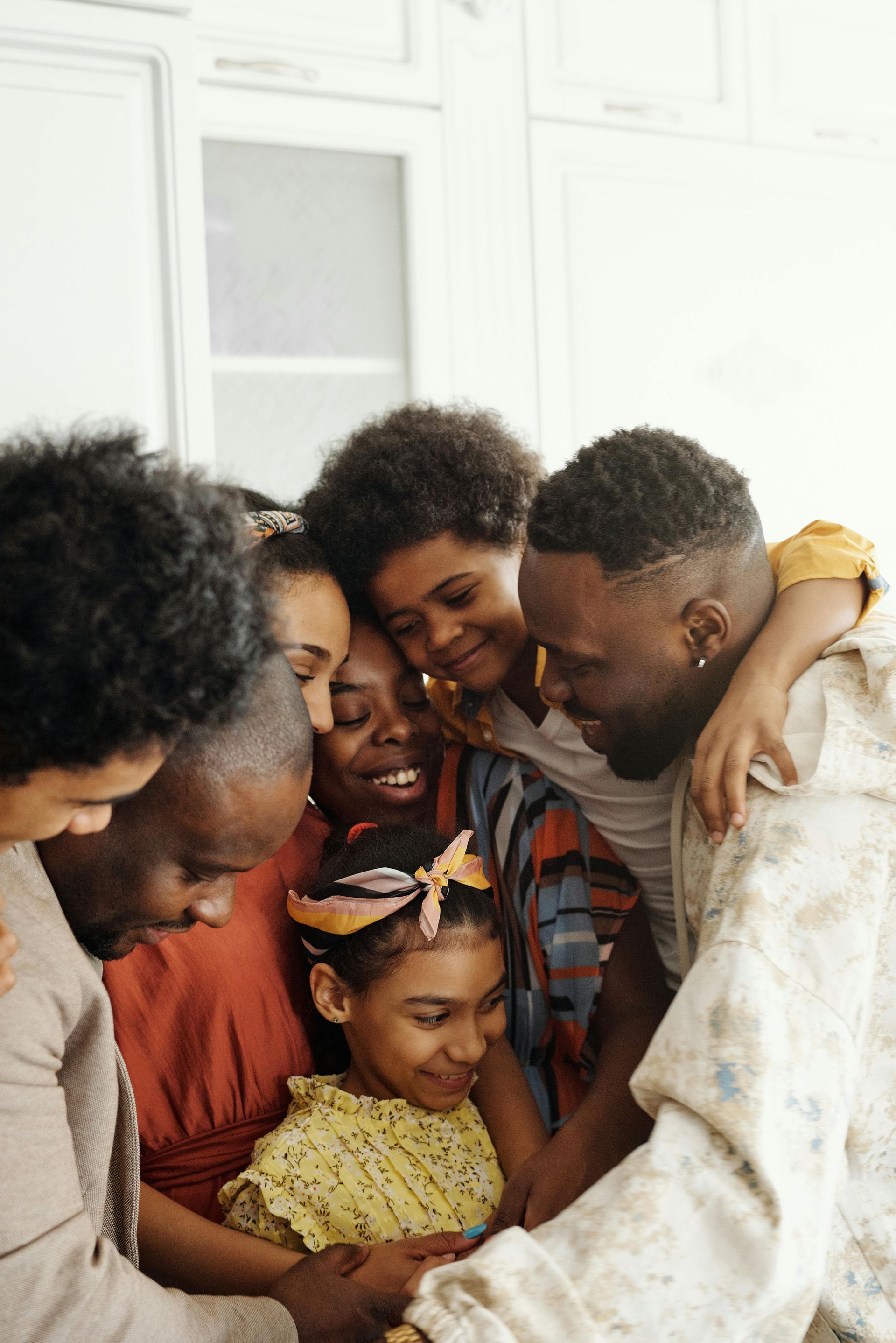 Family hugging together indoors, smiling and leaning in close in a bright white room