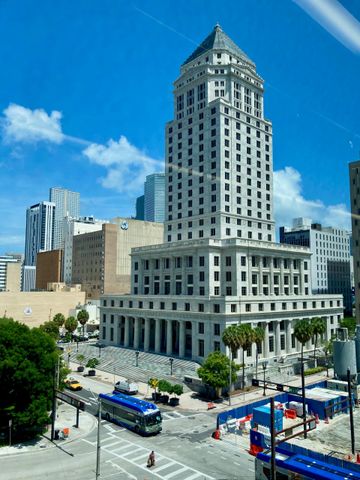 Tall white historic building downtown under a bright blue sky, with buses and construction barriers at street level
