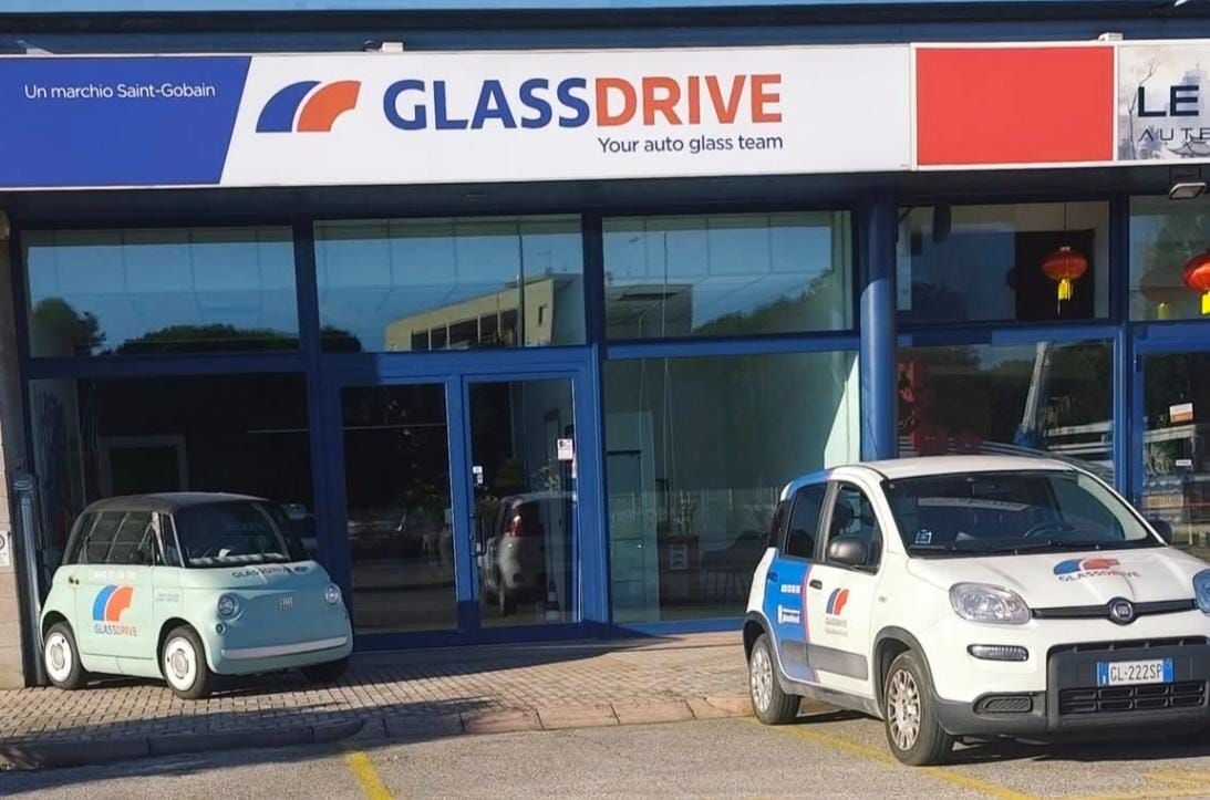 Negozio GlassDrive con due auto parcheggiate all'esterno. Insegna blu e bianca, vetrina con porte in vetro.