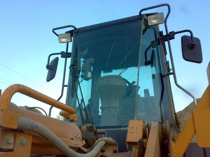 Primo piano della cabina di un veicolo da costruzione giallo con parabrezza, specchietti e luci sullo sfondo del cielo azzurro.