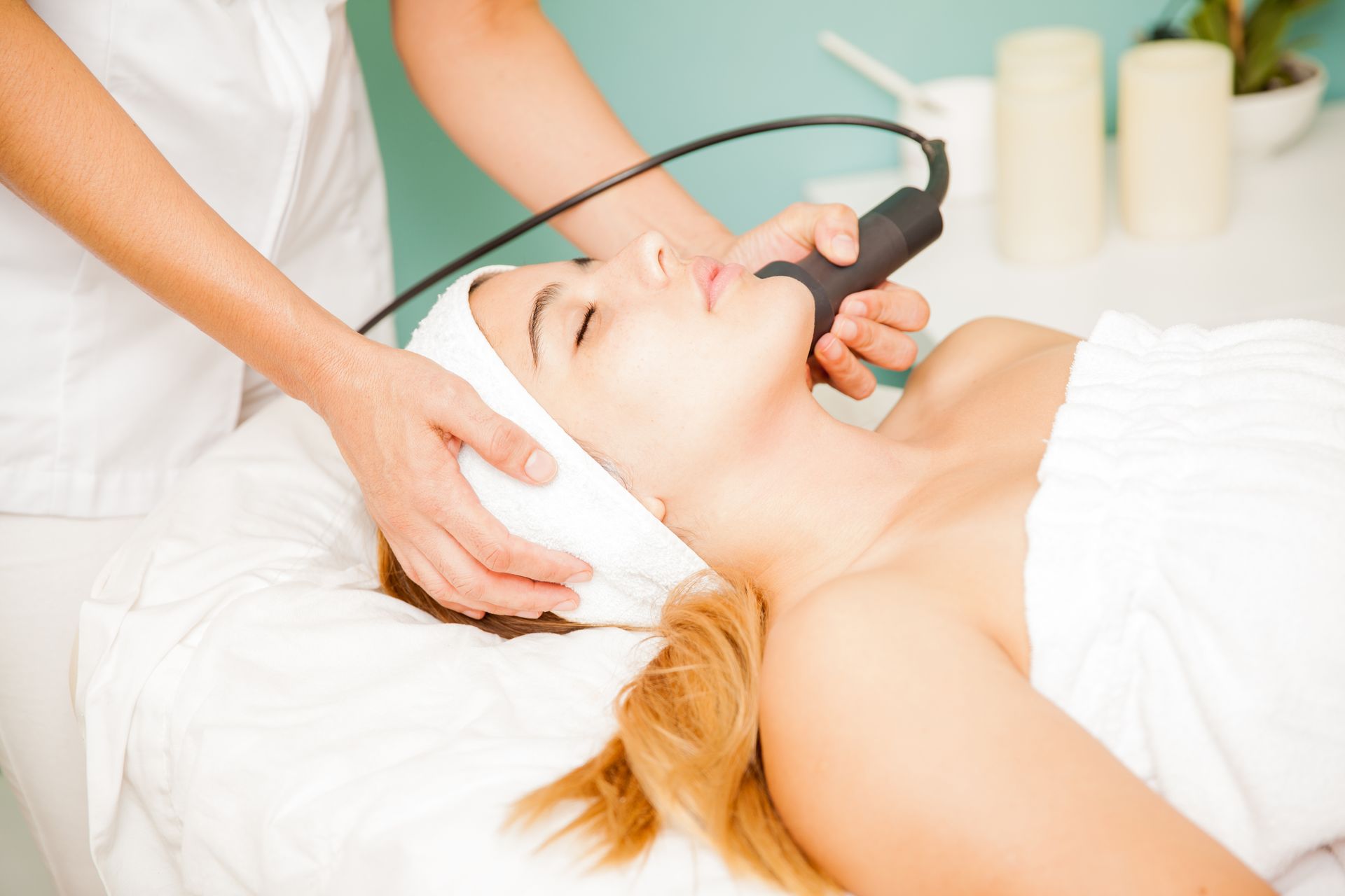 Woman receiving facial treatment in a spa. Therapist uses a device on her face.