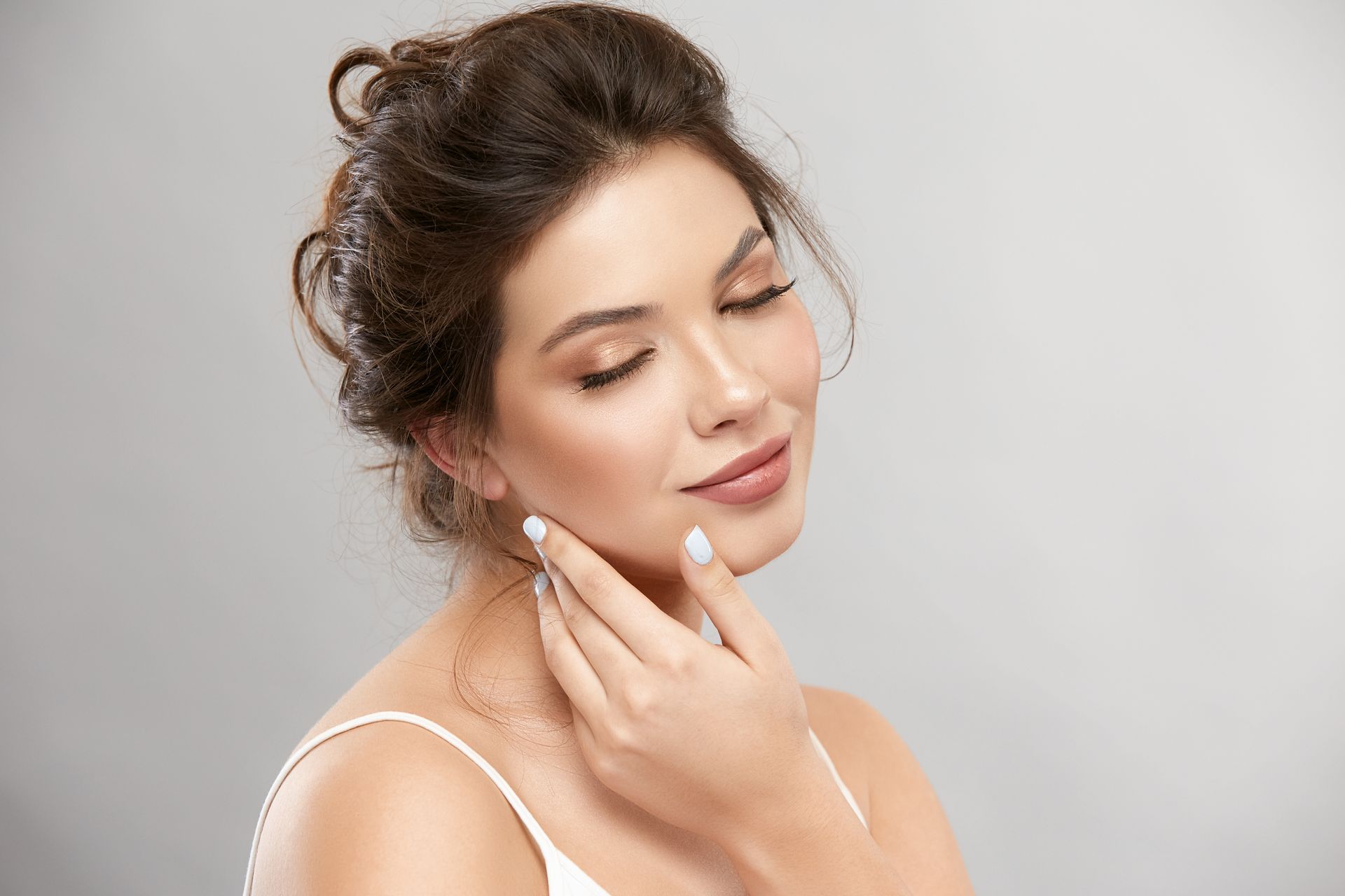 A woman is touching her face with her hand and smiling.