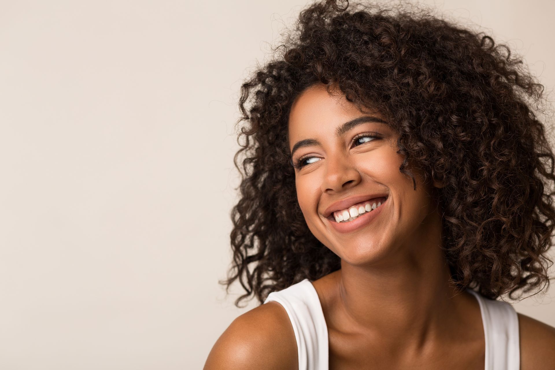 A woman with curly hair is smiling and looking to the side.