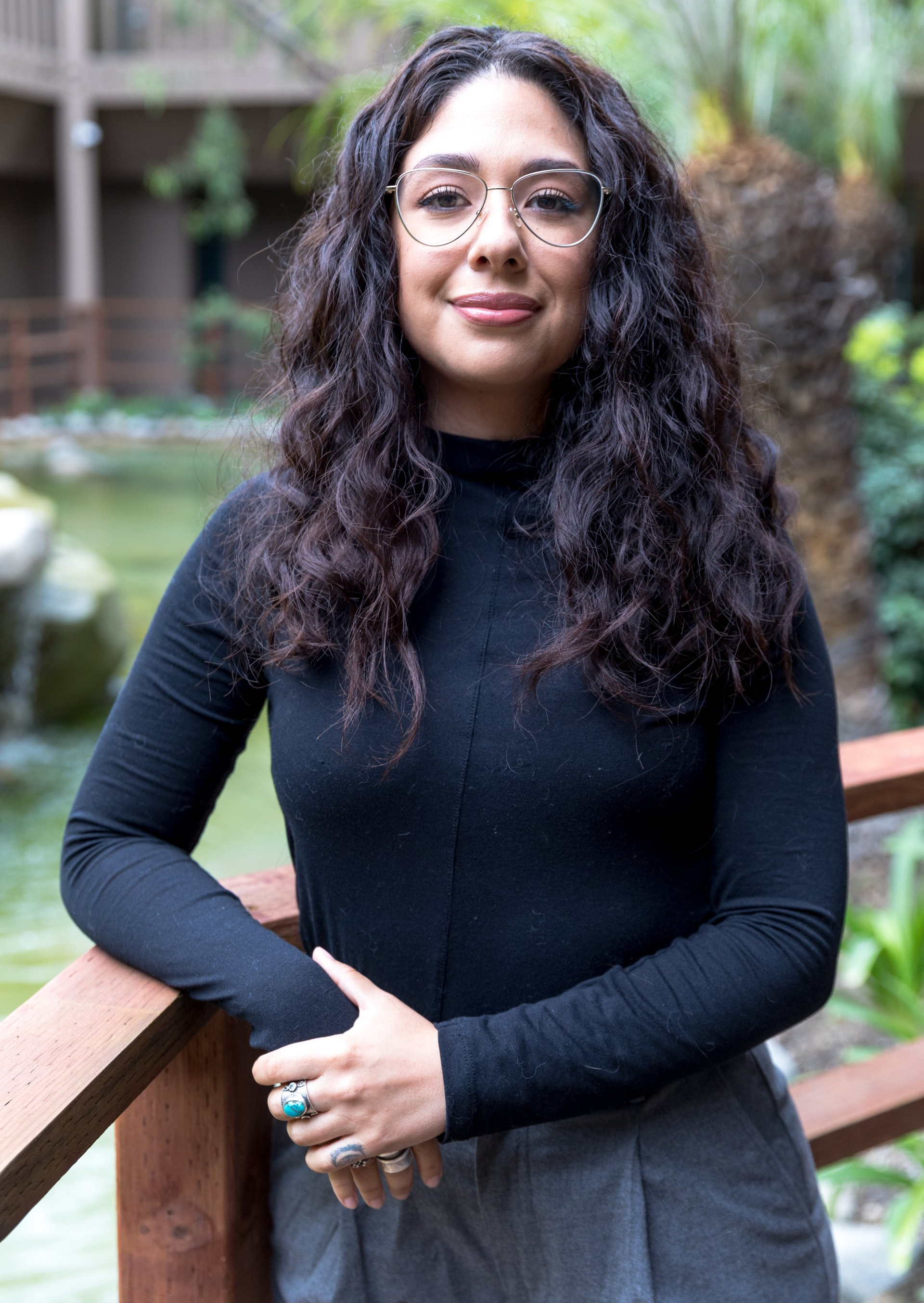 A woman wearing glasses and a black shirt is standing next to a wooden railing.