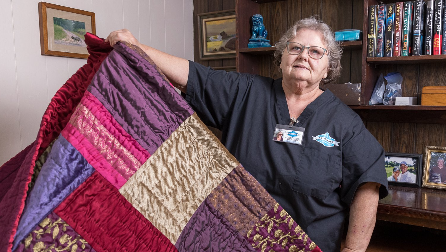 A woman in a black scrub top is holding a colorful quilt.