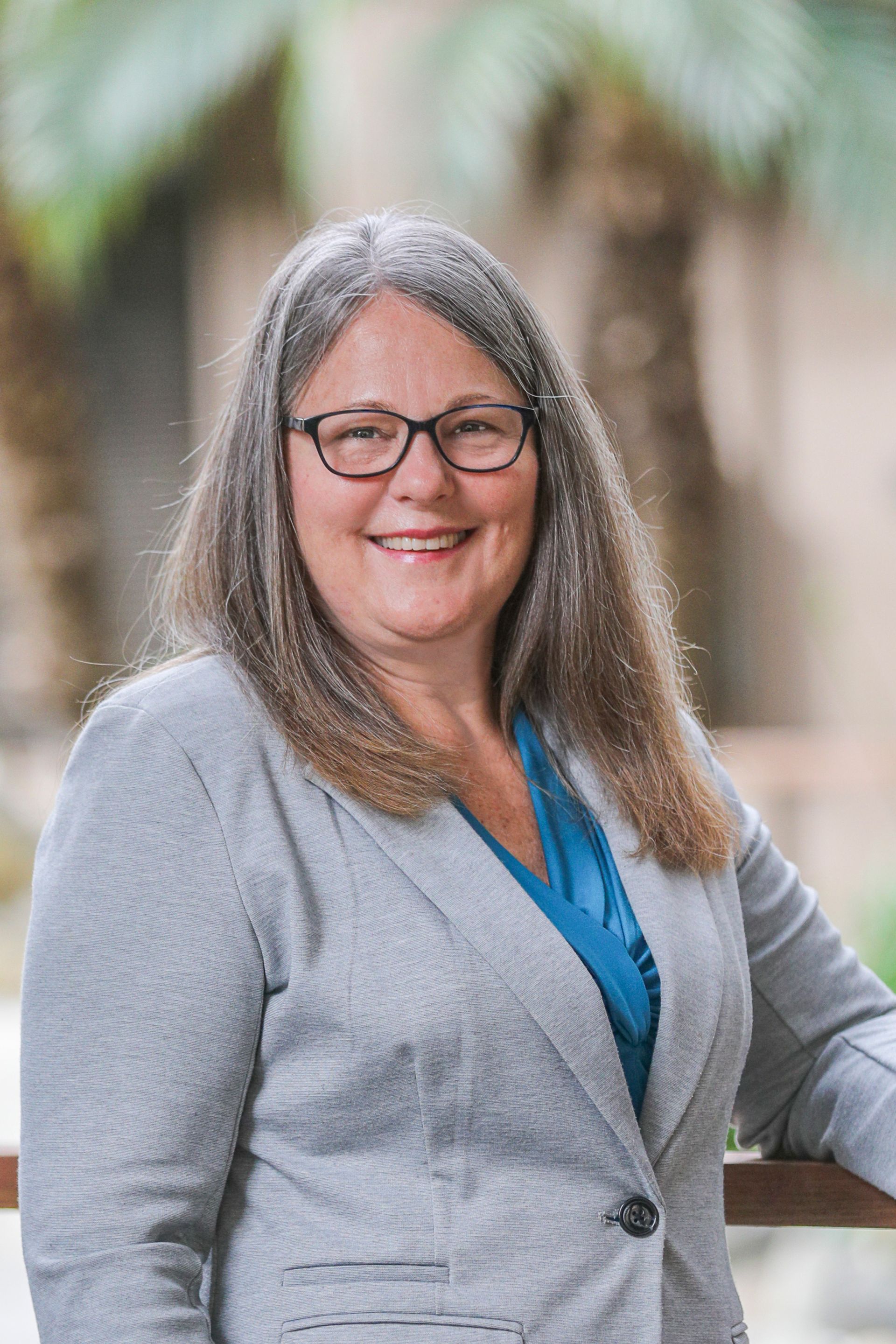 A woman wearing glasses and a gray jacket is smiling for the camera.