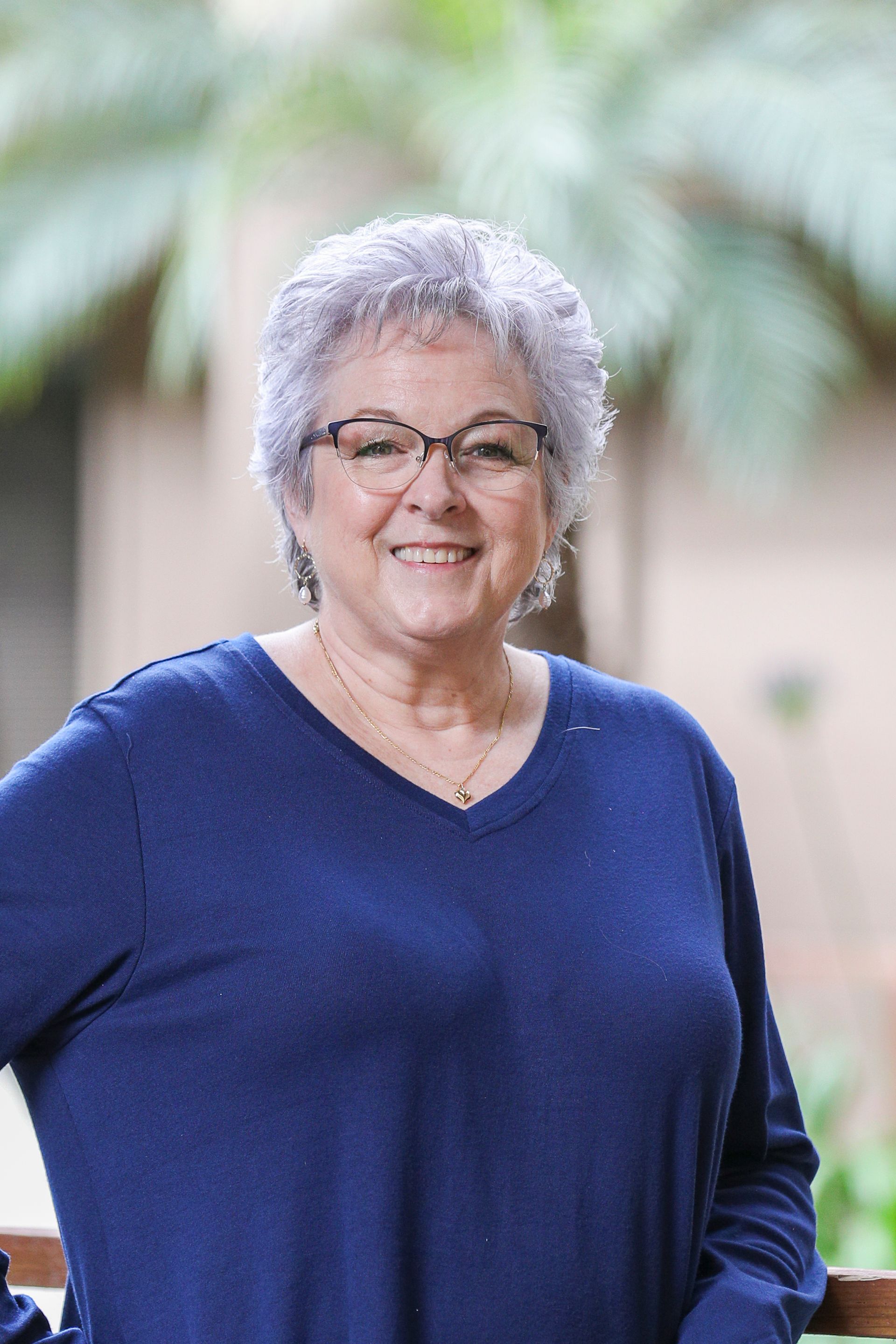 A woman wearing glasses and a blue shirt is smiling for the camera.