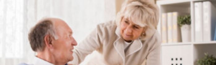 A woman is talking to an older man in a living room.